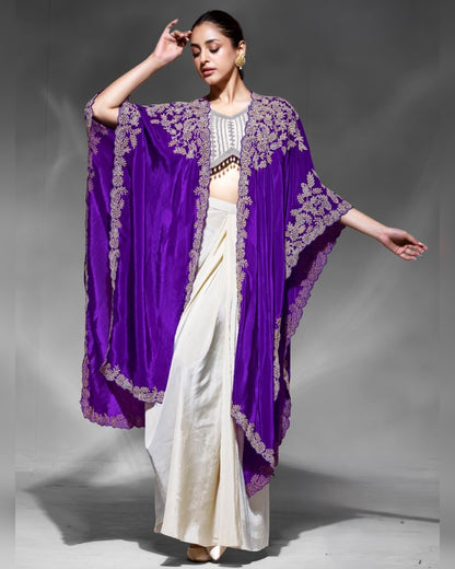 Woman wearing a white saree with a purple embroidered coverup on a gray background