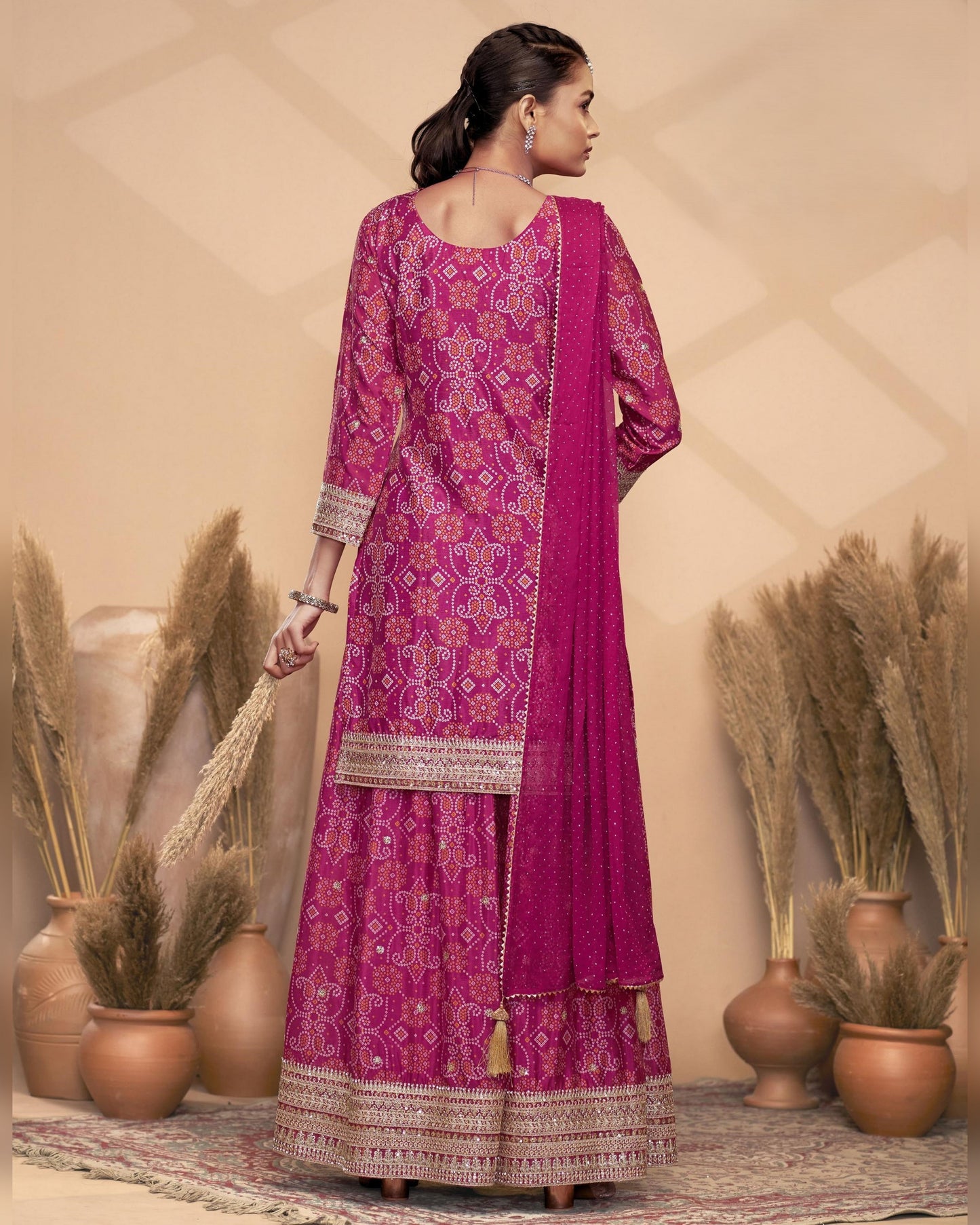 Woman wearing a pink embroidered traditional outfit with a beige background and decorative plants.