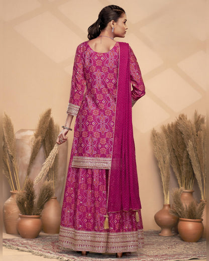 Woman wearing a pink embroidered traditional outfit with a beige background and decorative plants.