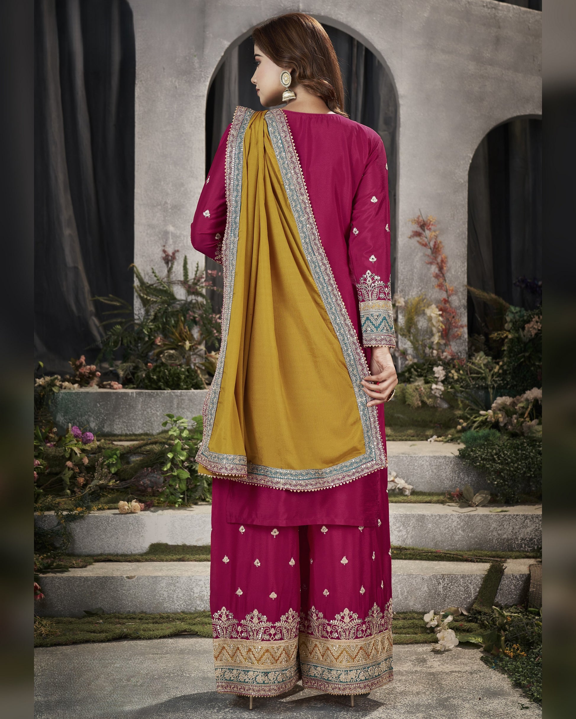 Woman wearing a traditional pink and yellow outfit with intricate patterns in an outdoor setting.