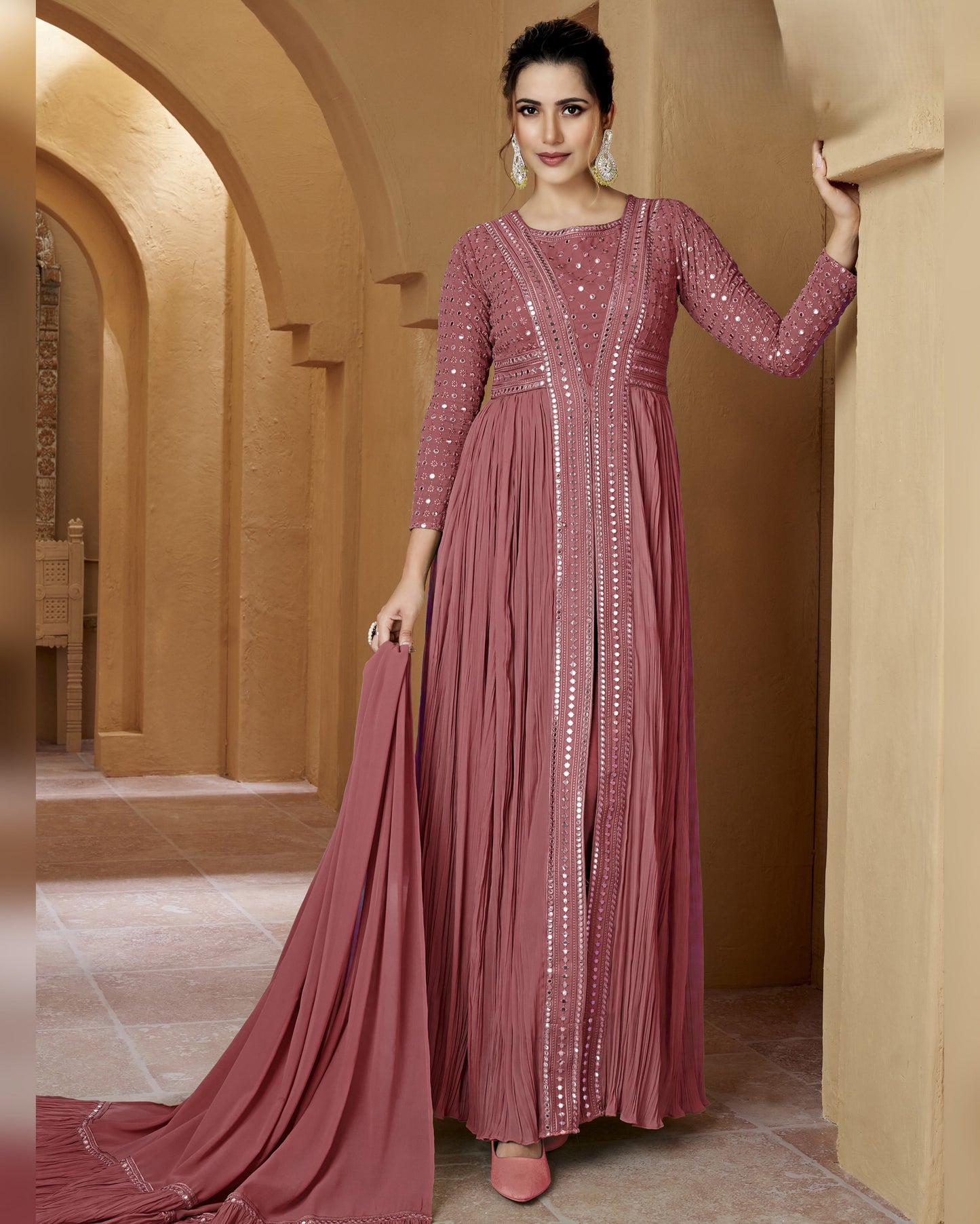 Woman in a long, elegant pink dress with intricate detailing in an ornate hallway.