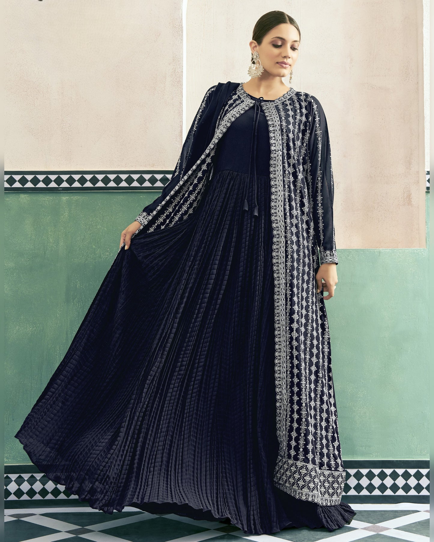 Woman wearing a dark blue traditional outfit with a patterned shawl against a decorative wall.