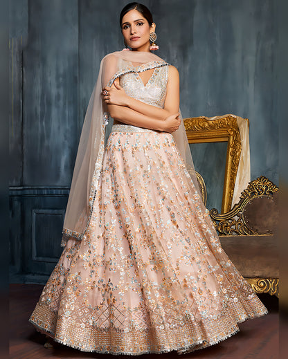 Woman in a beige embroidered lehenga with a gold frame in the background