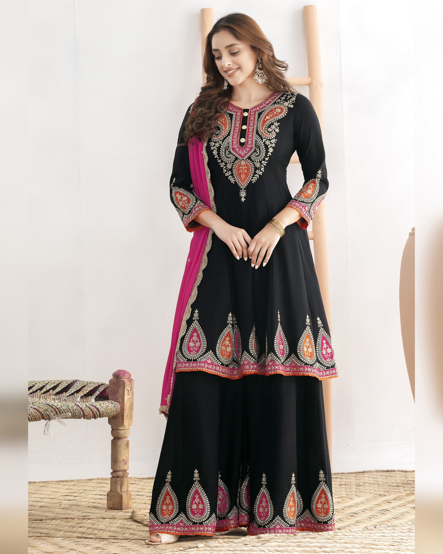 Woman wearing a black embroidered traditional outfit with a pink border on a white background