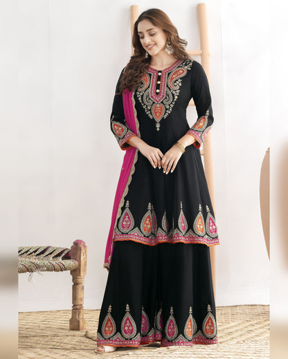 Woman wearing a black embroidered traditional outfit with a pink border on a white background