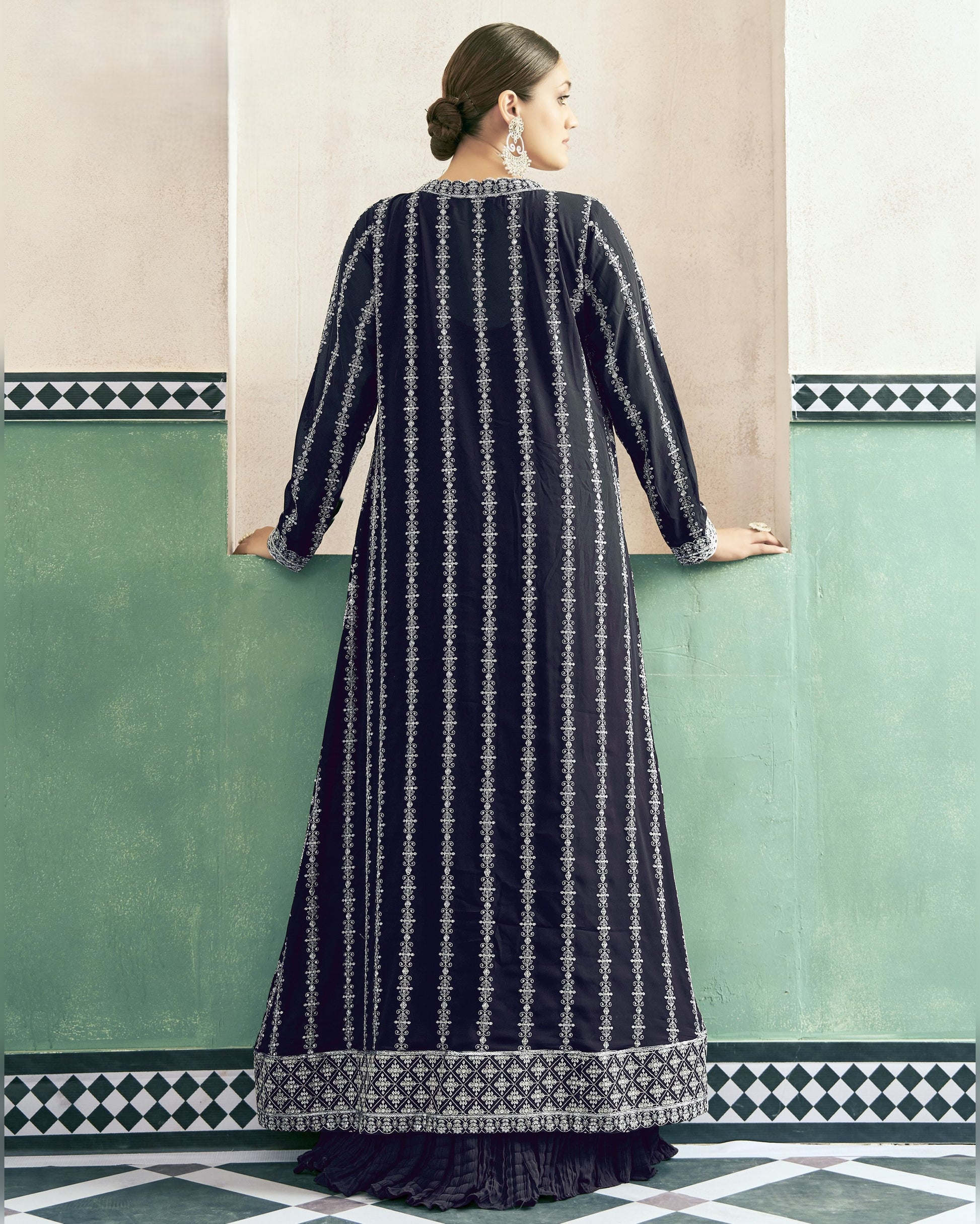 Woman wearing a long dark blue dress with white patterns against a light-colored wall.