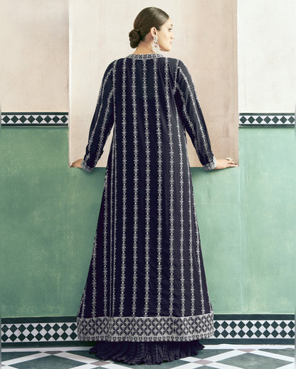 Woman wearing a long dark blue dress with white patterns against a light-colored wall.