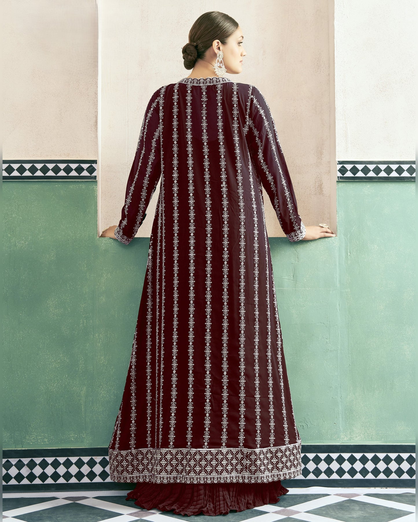 Woman wearing a long, patterned dress against a light-colored wall with geometric design.