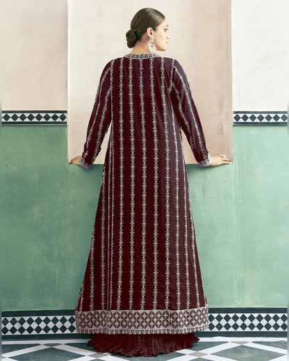 Woman wearing a long, patterned dress against a light-colored wall with geometric design.