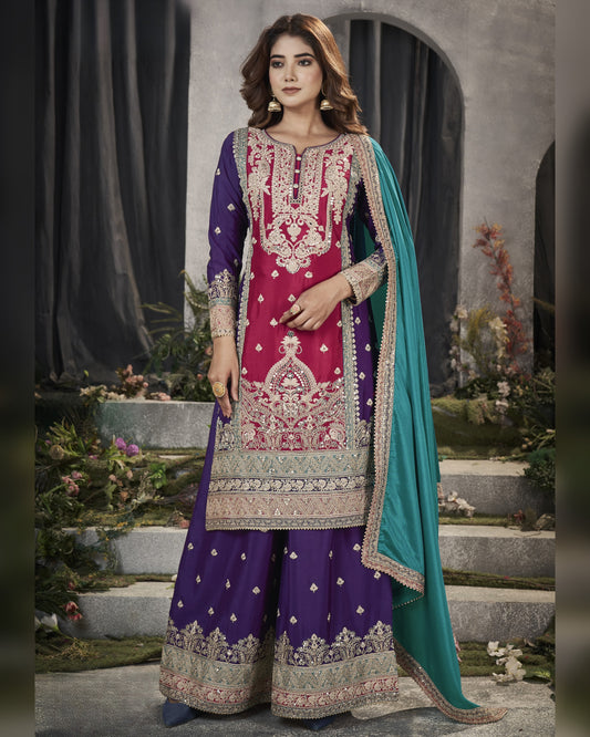 Woman wearing a traditional embroidered outfit with a purple and pink design, standing in an outdoor setting.