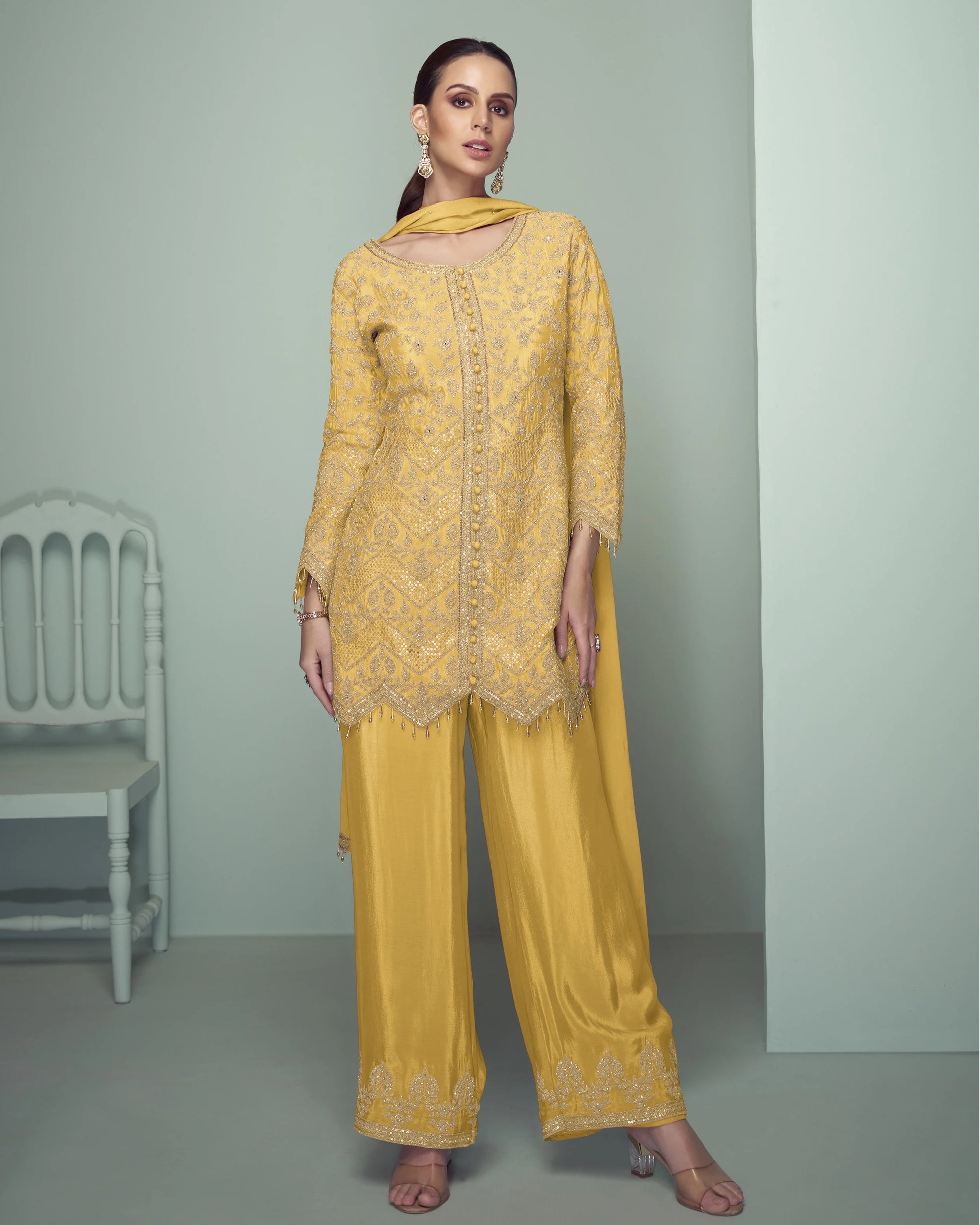 Woman wearing a yellow embroidered outfit with a matching dupatta against a gray background