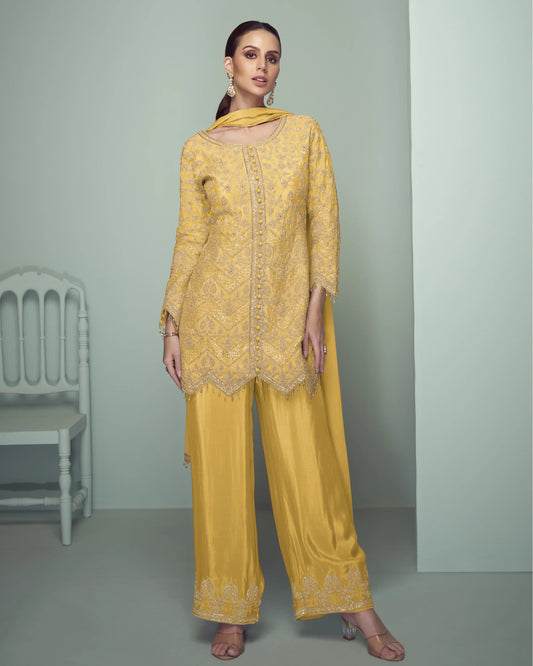 Woman wearing a yellow embroidered outfit with a matching dupatta against a gray background