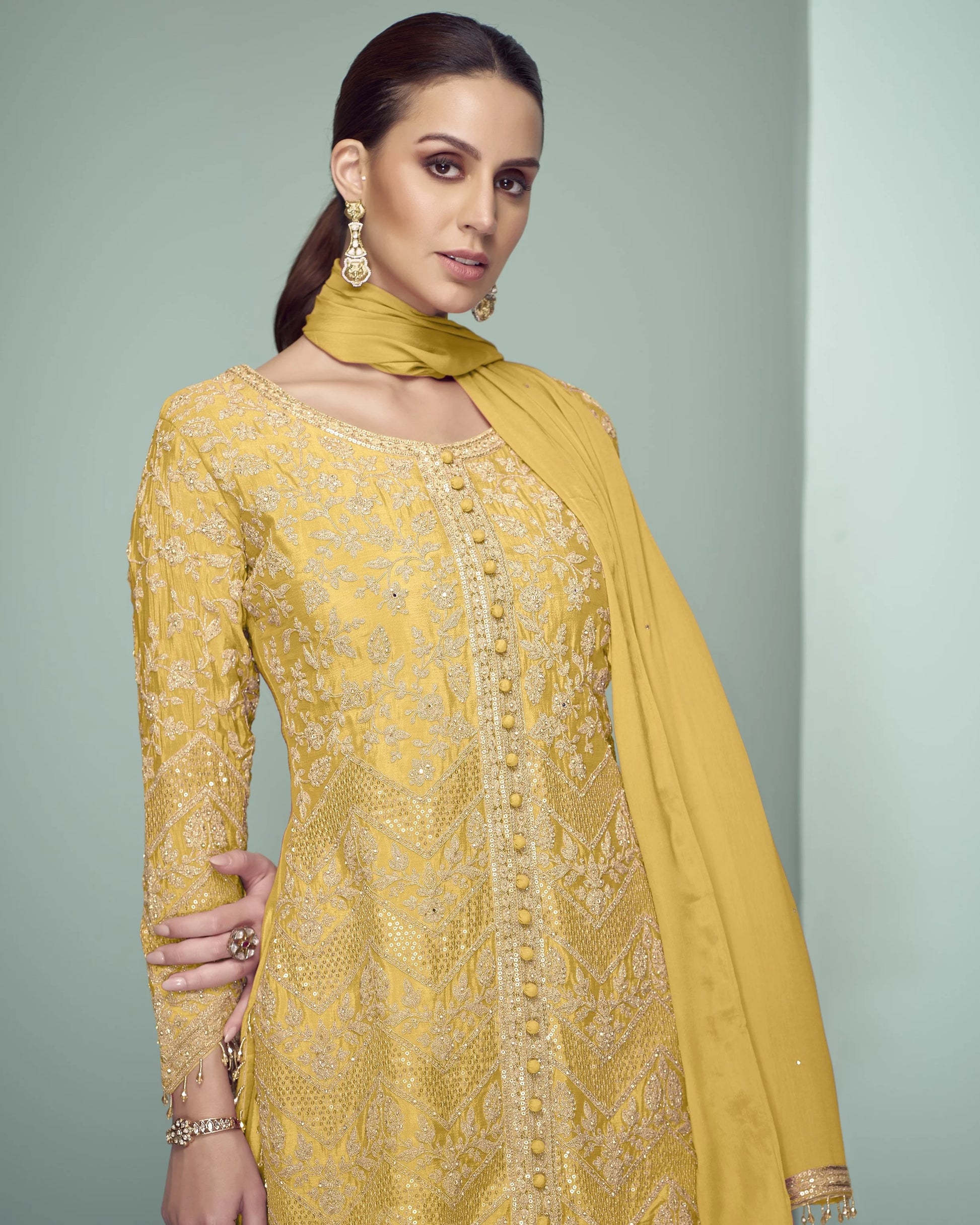 Woman wearing a yellow embroidered outfit with a matching dupatta against a gray background